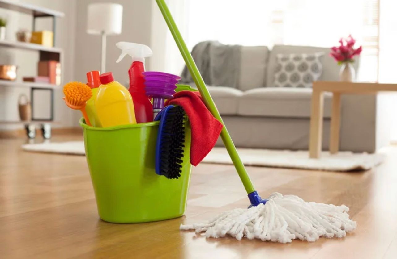 Cleaning supplies in a bucket, with a mop on living room floor 